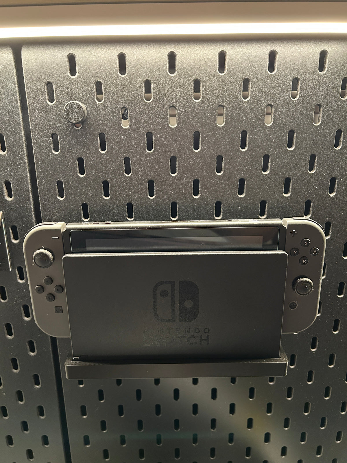 Cache fixation noir clipsé sur un panneau SKÅDIS, support Nintendo Switch en dessous